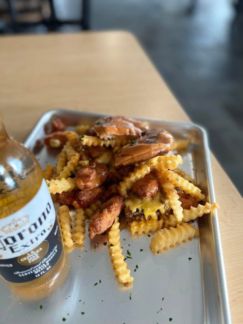 A tray of crinkle-cut fries topped with cheese and chicken, alongside a bottle of Corona beer.