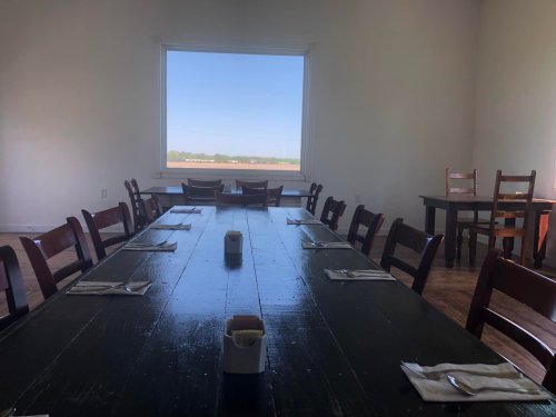 A spacious dining room with a long wooden table, chairs, and a large window overlooking a green landscape.