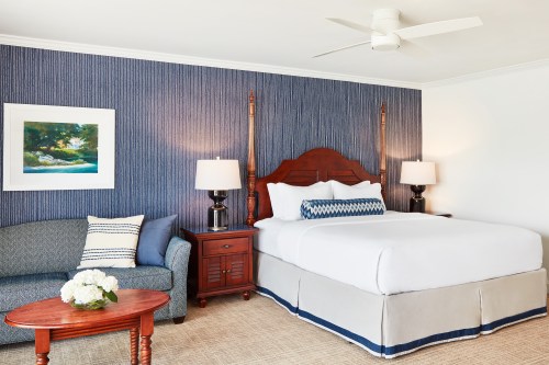 A cozy hotel room featuring a king bed, blue accent wall, sofa, and two lamps on nightstands.