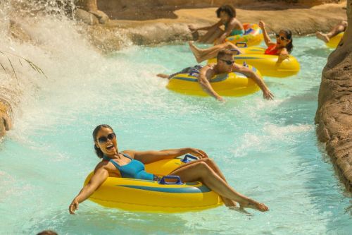 A group of people enjoying a lazy river on yellow inner tubes, splashing water and relaxing under the sun.