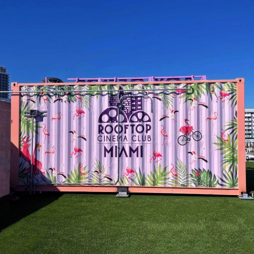 Colorful container with tropical designs and flamingos, featuring "Rooftop Cinema Club Miami" against a clear blue sky.