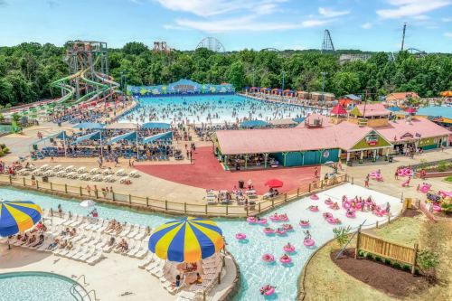 A vibrant water park scene with pools, slides, and crowds enjoying the sunny day amidst lush greenery.