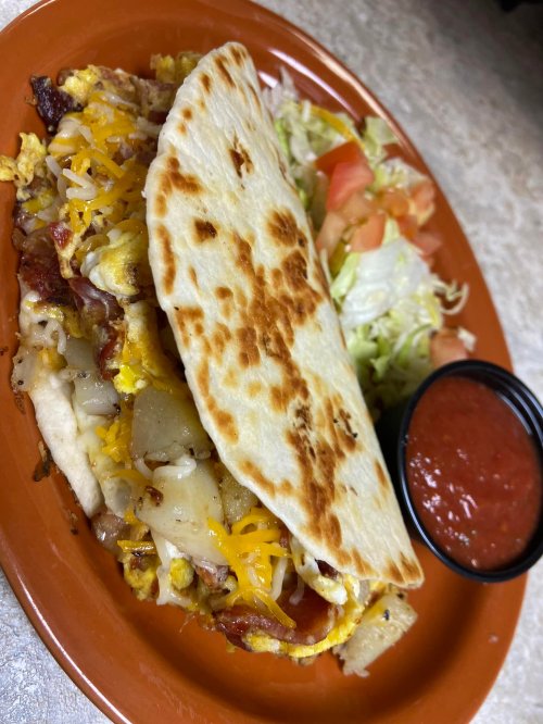 A plate featuring a stuffed tortilla with cheese, bacon, and vegetables, accompanied by a side salad and salsa.