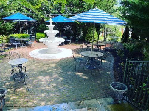 A serene outdoor patio with a fountain, surrounded by tables and blue-striped umbrellas under lush greenery.