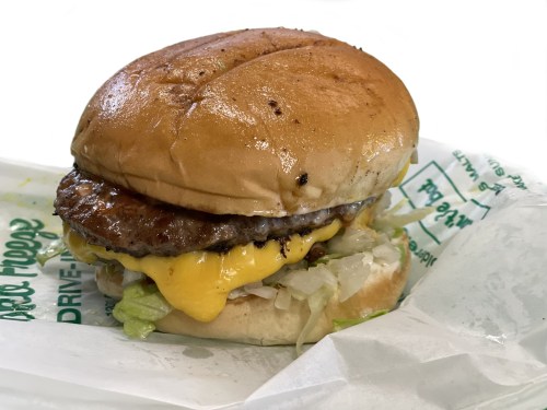 A juicy cheeseburger with lettuce, melted cheese, and a toasted bun, served on a wrapper.