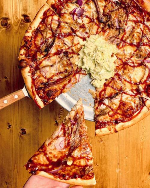 A pizza topped with barbecue sauce, onions, and a side of coleslaw, with a slice being held.