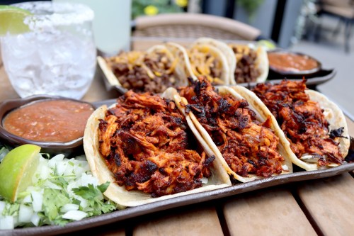 A platter of tacos filled with shredded meat, served with salsa, lime, onions, and cilantro, alongside a drink.