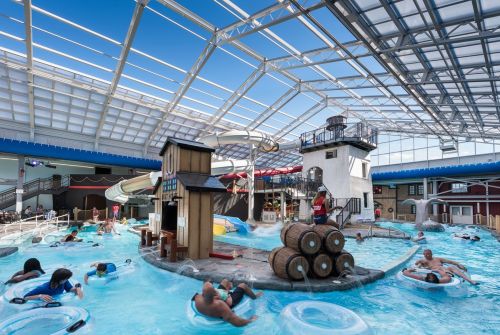 Indoor water park featuring a large pool, water slides, and a lighthouse structure, with people enjoying the water.