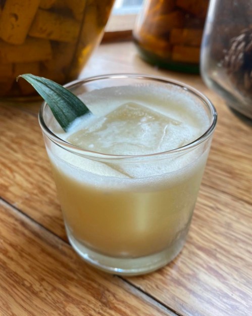 A refreshing cocktail in a glass, garnished with a green leaf, sitting on a wooden table.