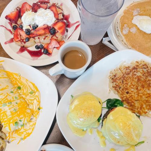 A table spread with pancakes, eggs Benedict, hash browns, a fruit dessert, and drinks.