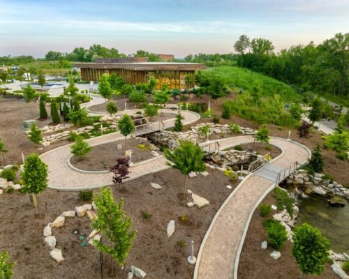 A landscaped park with winding pathways, trees, and a modern building in the background under a clear sky.