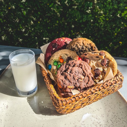 A woven basket filled with assorted cookies and a glass of milk, set against a green background.