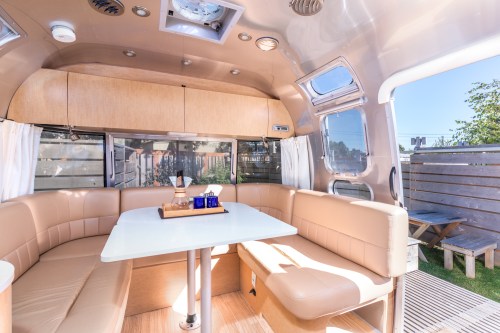 Interior of a modern Airstream trailer featuring a cozy seating area and a table, with large windows and natural light.