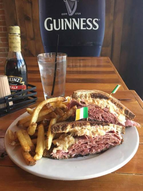 A hearty sandwich with corned beef and sauerkraut, served with fries and a drink, set against a rustic wooden backdrop.