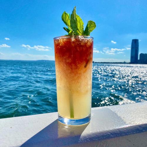 A refreshing cocktail with mint leaves sits on a railing, overlooking a sparkling blue sea and a clear sky.