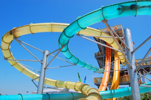 Colorful water slides twist and turn against a clear blue sky, with a tall structure in the background.