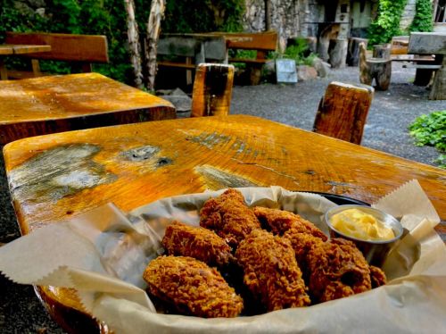 A plate of crispy fried chicken wings with a side of butter, set on a rustic wooden table in a lush outdoor setting.