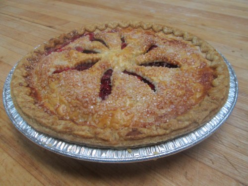 A freshly baked pie with a golden crust and a lattice top, sprinkled with sugar, on a wooden surface.