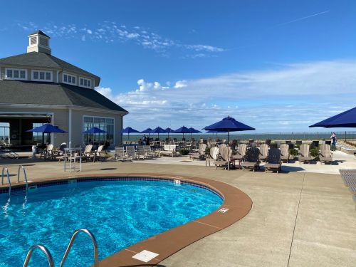 A sunny pool area with lounge chairs and umbrellas, overlooking a calm body of water and a blue sky.