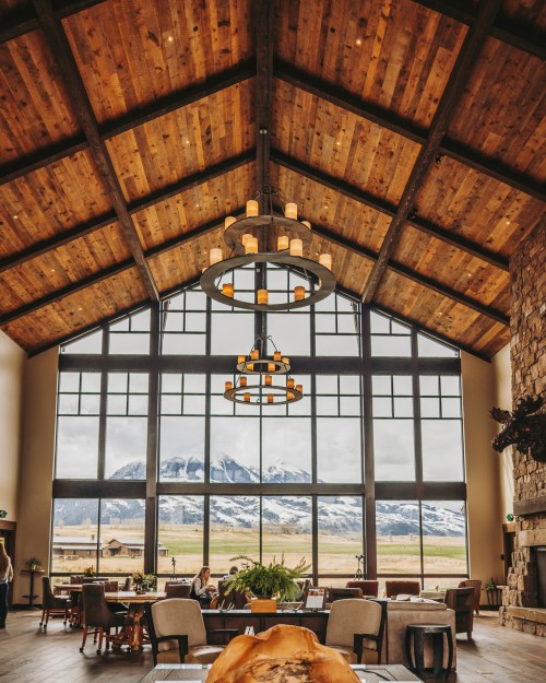 A spacious lodge interior with wooden beams, large windows showcasing mountains, and cozy seating areas.
