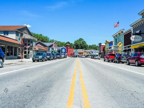 A sunny street view of a small town with colorful buildings and parked cars lining both sides of the road.
