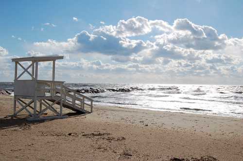 A lifeguard tower on a sandy beach with waves and cloudy skies in the background.