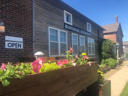 Exterior of Ronneburg Restaurant with an "Open" sign and colorful flowers in a planter. Clear blue sky above.