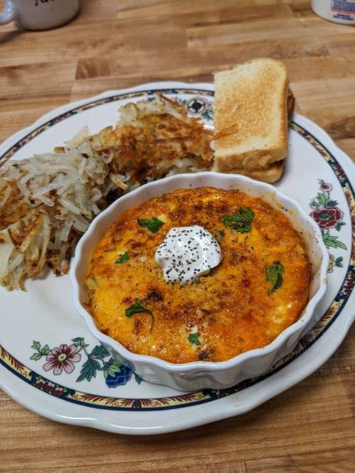 A baked egg dish topped with sour cream, served with hash browns and toast on a decorative plate.