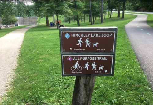 Signpost indicating the Hinckley Lake Loop and All Purpose Trail distances, surrounded by greenery and pathways.