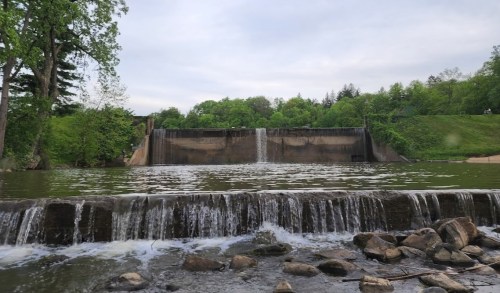 A serene view of a dam with cascading water, surrounded by lush greenery and a calm river.