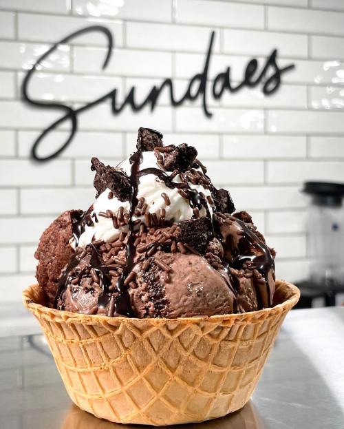 A large ice cream sundae in a waffle bowl, topped with whipped cream, chocolate syrup, and cookie pieces.