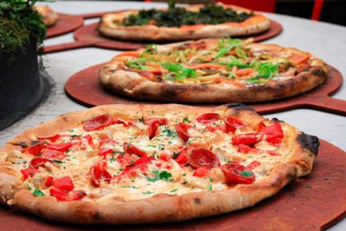 Three pizzas on wooden peels: one with pepperoni and tomatoes, another with greens, and a third with mixed vegetables.