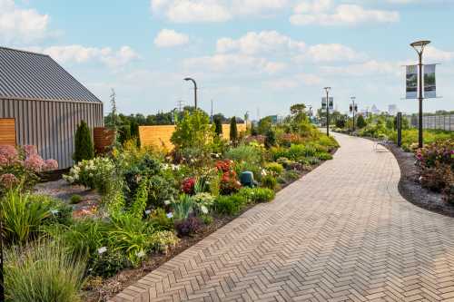 A landscaped pathway lined with colorful flowers and greenery, leading to a modern building under a blue sky.