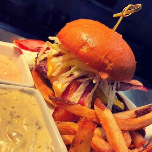 A juicy burger with lettuce, cheese, and bacon, served with fries and dipping sauces on a plate.