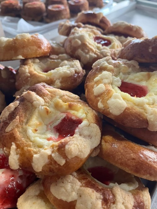 A close-up of freshly baked pastries with a creamy filling and a dollop of red fruit jam on top.