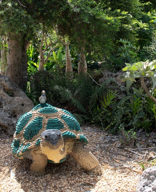 A large turtle sculpture made of colorful blocks, with a small bird perched on its back, surrounded by lush greenery.