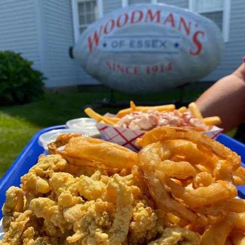 A blue tray filled with fried seafood, coleslaw, and dipping sauces, with a restaurant sign in the background.