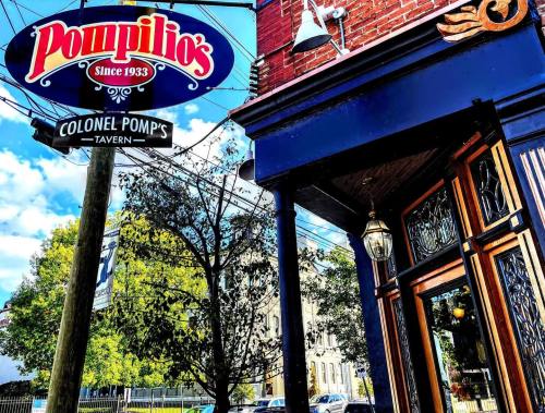 Sign for Pompilio's since 1933 and Colonel Pomp's Tavern, with a blue building and trees in the background.