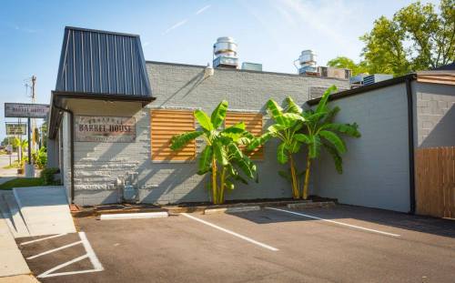 Exterior view of a building with a sign reading "Barrel House," featuring palm trees and a paved parking area.