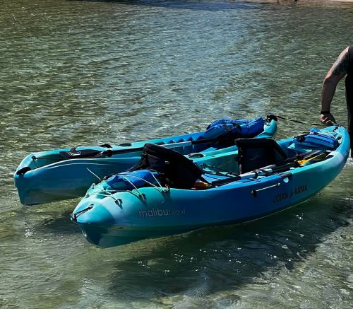 Two blue kayaks on clear water, with a person pulling one kayak towards the shore.