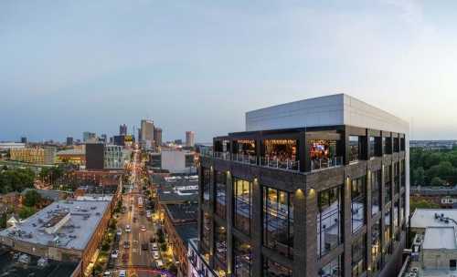 Aerial view of a city skyline at dusk, featuring a modern building and bustling streets below.