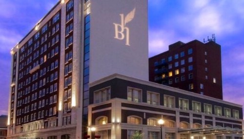 A modern hotel building illuminated at dusk, featuring a logo and a colorful sky in the background.