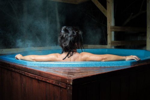 A woman relaxes in a hot tub, steam rising around her in a serene, dimly lit outdoor setting.