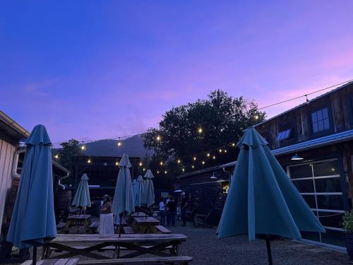 Outdoor dining area at dusk, featuring tables with umbrellas and string lights against a colorful sky.