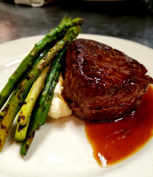 A plated meal featuring a juicy steak, grilled asparagus, and creamy mashed potatoes with a rich sauce.