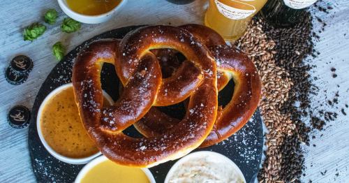A plate of soft pretzels with various dipping sauces, surrounded by beer and scattered grains.