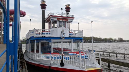 A colorful riverboat docked at a pier, with a cloudy sky and water in the background.