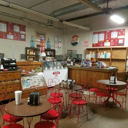 A cozy diner interior with red metal chairs, wooden tables, a counter, and a menu on the wall.