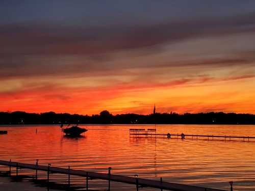 A vibrant sunset over a lake, with orange and purple hues reflecting on the water and silhouettes of docks.