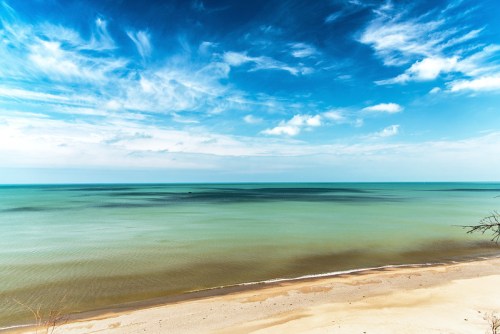 A serene beach scene with calm turquoise waters and a clear blue sky, featuring soft clouds and a sandy shore.